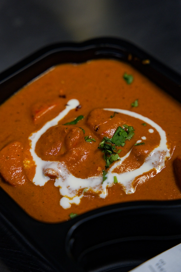 Indisk butter chicken servert i takeaway-boks, toppet med krem og frisk koriander.
